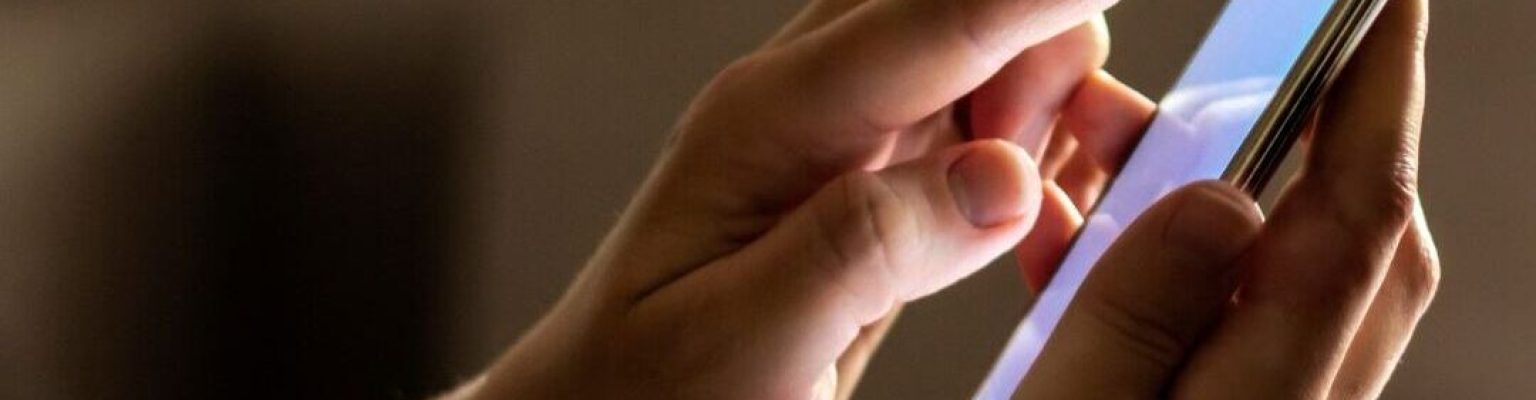 Hands tapping on a glowing smartphone screen in a dimly lit room, symbolizing late-night access to 24/7 nurse support for pregnancy centers.