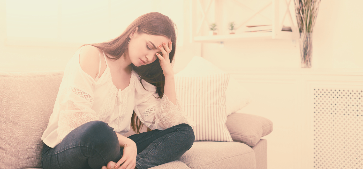 Women sitting on sofa, looking sad, head in hand, obviously distraught, struggling with post abortion stress.
